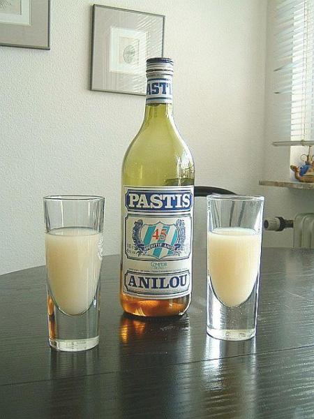 Bottle of pastis with two filled glasses.