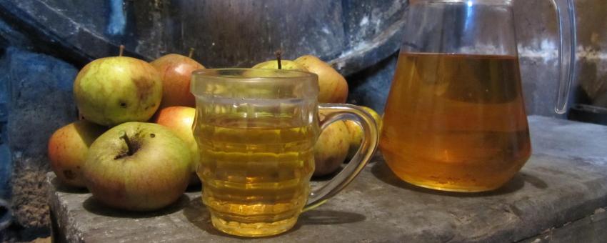 A pitcher and a mug of dry cider next to a oak barrel in a Normandy cellar