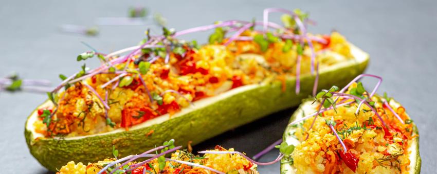 Baked zucchini with vegetables and couscous on a black background with micro green cabbage