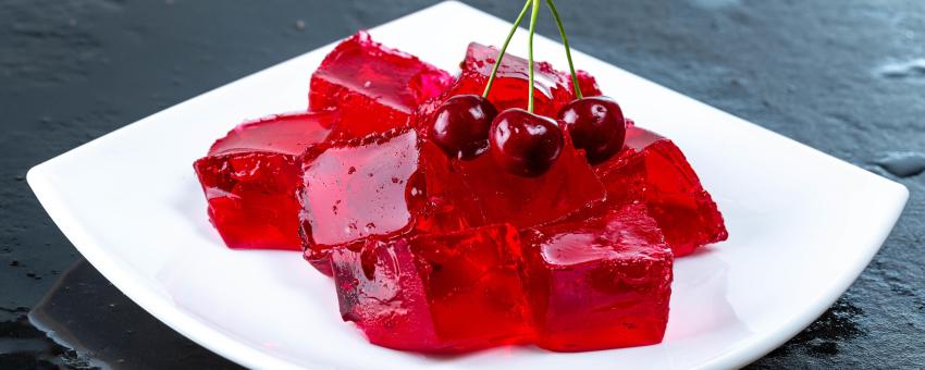 Tasty jelly cubes on white plate with cherry