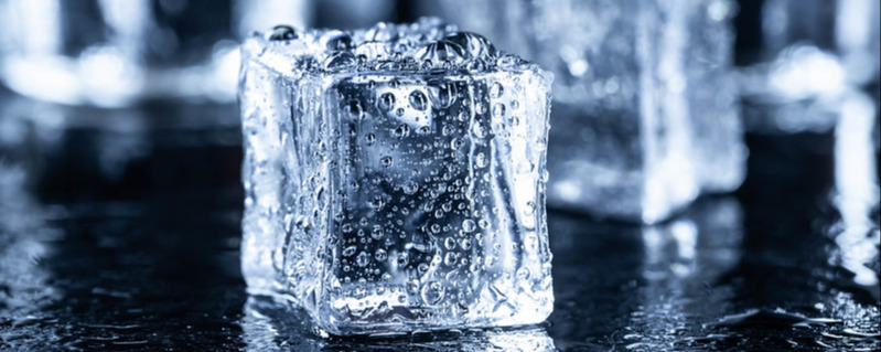 Ice cubes with water drops and vodka glasses in the background